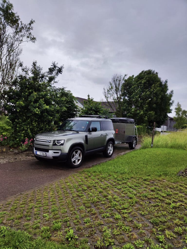 Der Offroadanhänger Corse setzt neue Maßstäbe für Abenteurer, die maximale Freiheit und Funktionalität suchen. Als hochwertiger Zeltanhänger wurde er speziell für anspruchsvolle Touren entwickelt und überzeugt durch robuste Bauweise, intelligente Ausstattung und modernes Design. Die seitliche Tür sorgt für einen besonders komfortablen Zugang zum Innenraum und ermöglicht eine flexible Nutzung des Stausystems – ideal für Camping, Expeditionen oder Wochenendtrips. Dank der integrierten Kugelaufnahme für Fahrradträger lässt sich der Offroadanhänger Corse problemlos um zusätzliche Transportkapazität erweitern. Perfekt für alle, die ihre Bikes auch abseits befestigter Wege einsetzen möchten. Die stabile Reling R.O.Rack eignet sich optimal zur Montage eines Dachzelts und verwandelt den Offroadanhänger in eine vollwertige Outdoor-Base für mehrtägige Abenteuer. Optisch besticht der Anhänger mit einer exklusiven Lackierung in Land Rover Pangea Grün – ein echter Hingucker, der Robustheit und Stil vereint. Für maximale Unabhängigkeit verfügt der Zeltanhänger über eine vollständige 230-Volt-Elektroinstallation, die sämtliche Camping- und Ladegeräte zuverlässig versorgt. Ergänzt wird das Setup durch moderne LED-Fahrzeugbeleuchtung, die für beste Sichtbarkeit und maximale Energieeffizienz sorgt – selbst unter härtesten Offroad-Bedingungen.